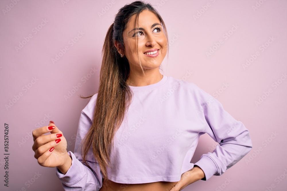 Young beautiful sport woman wearing sweatshirt over pink isolated background looking away to side with smile on face, natural expression. Laughing confident. Young beautiful sport woman wearing sweatshirt over pink isolated background looking away to side with smile on face, natural expression. Laughing confident.
