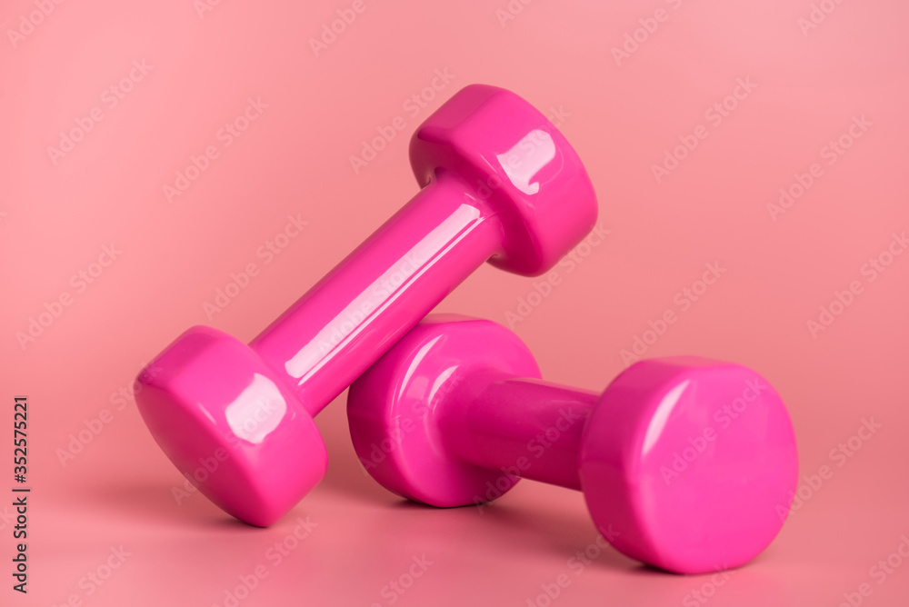 Workout concept. Close-up photo of two pink dumbbells isolated on pastel pink background Workout concept. Close-up photo of two pink dumbbells isolated on pastel pink background