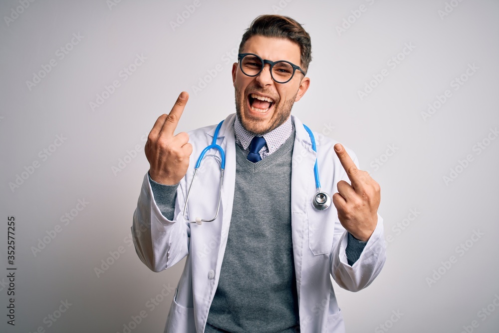 Young doctor man with blue eyes wearing medical coat and stethoscope over isolated background Showing middle finger doing fuck you bad expression, provocation and rude attitude. Screaming excited Young doctor man with blue eyes wearing medical coat and stethoscope over isolated background Showing middle finger doing fuck you bad expression, provocation and rude attitude. Screaming excited