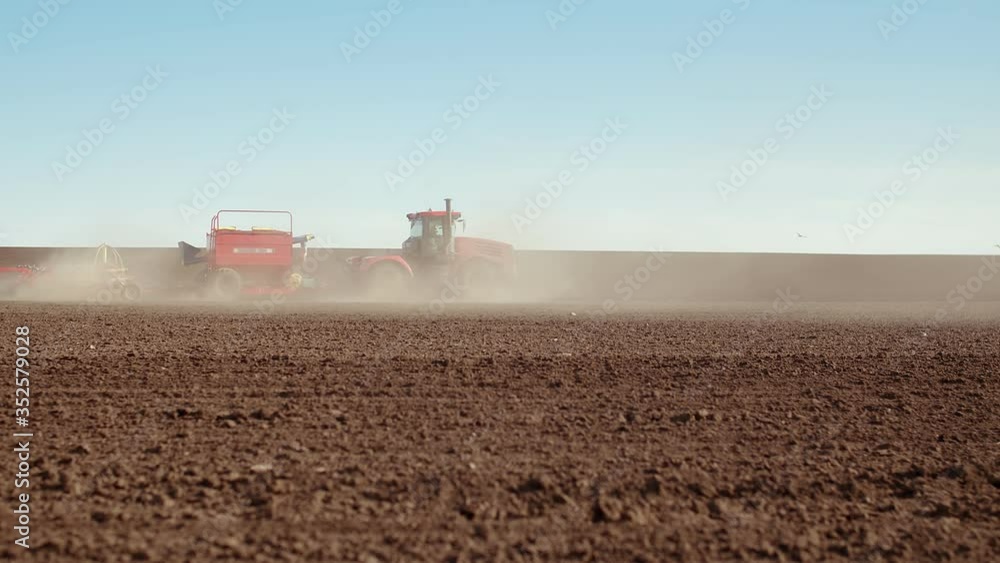 Side view of a tractor, a tank with seeds and a seeder passing through the field sowing seeds. Sowing a field of corn with a tractor Side view of a tractor, a tank with seeds and a seeder passing through the field sowing seeds. Sowing a field of corn with a tractor