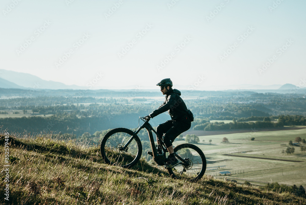 Young athletic man on an e-bike pedaling up the hill with a beautiful view. Amazing nature for meditating, hiking, biking and exploring.