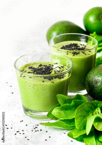 Green smoothie of avocado, spinach and seeds in glasses and spinach leaves on a gray concrete table. Healthy eating, raw food diet and vegan food. Green vegetables smoothie.