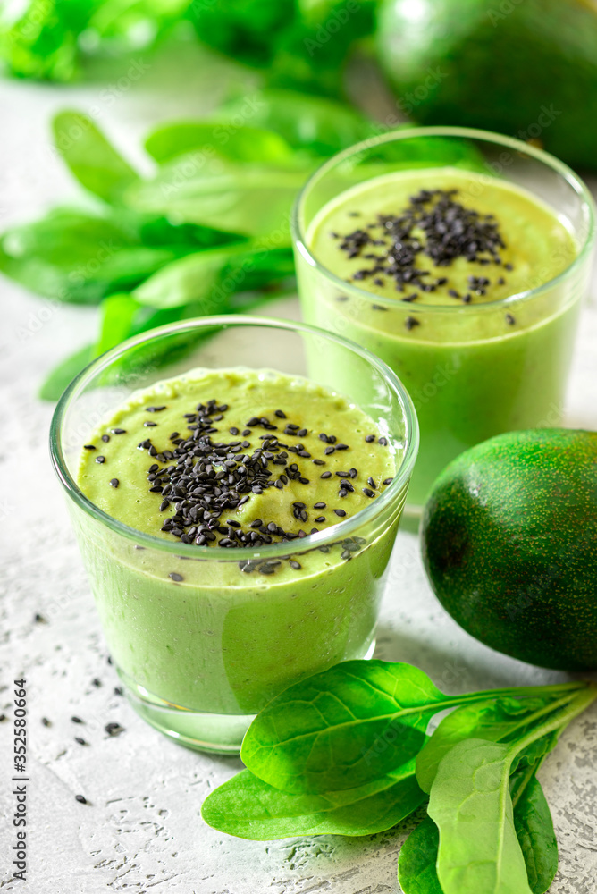 Green smoothie of avocado, spinach and seeds in glasses and spinach leaves on a gray concrete table. Healthy eating, raw food diet and vegan food. Green vegetables smoothie. Green smoothie of avocado, spinach and seeds in glasses and spinach leaves on a gray concrete table. Healthy eating, raw food diet and vegan food. Green vegetables smoothie.