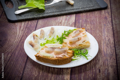 sandwich with salad, herring and herbs with onions in a plate