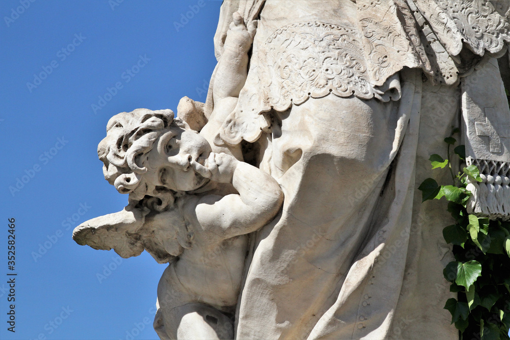 Detail of statue. Little angel in the foreground, blue sky in the background.