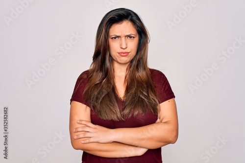 Young hispanic woman wearing casual t-shirt standing over isolated background skeptic and nervous, disapproving expression on face with crossed arms. Negative person.