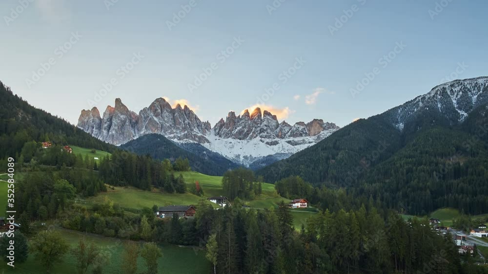 Time lapse of a beautiful red sunset illuminating The Dolomites mountain peaks overlooking a small church and houses surrounded by green forest and countryside in St Magdalena, Italy Time lapse of a beautiful red sunset illuminating The Dolomites mountain peaks overlooking a small church and houses surrounded by green forest and countryside in St Magdalena, Italy
