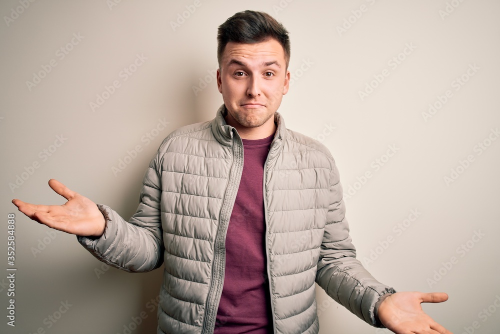 Young handsome caucasian man wearing casual winter jacket standing over isolated background clueless and confused expression with arms and hands raised. Doubt concept. Young handsome caucasian man wearing casual winter jacket standing over isolated background clueless and confused expression with arms and hands raised. Doubt concept.