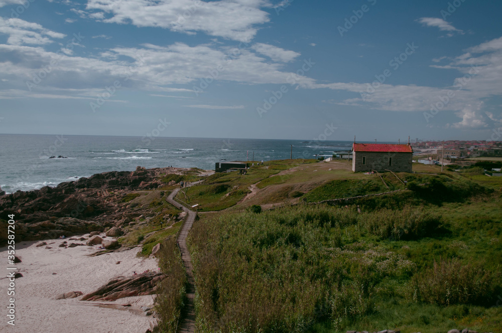 The old Stone Chapel on the hill above the ocean is covered with green grass. Below the white sand beach