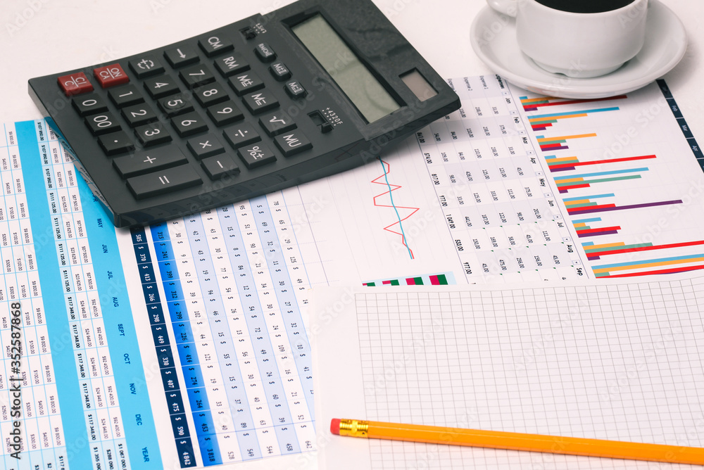 A table with the company's financial indicators, a calculator, a Cup of coffee, and a Notepad with a copy of the space. Earnings and income of the enterprise. Office Desk of an accountant, analyst A table with the company's financial indicators, a calculator, a Cup of coffee, and a Notepad with a copy of the space. Earnings and income of the enterprise. Office Desk of an accountant, analyst