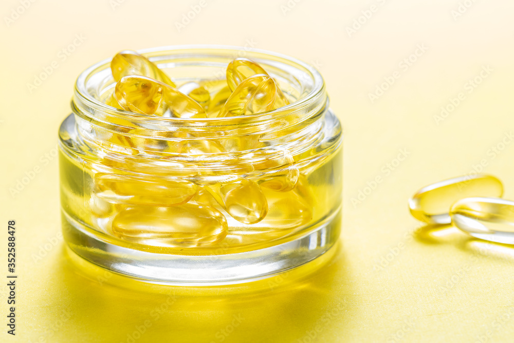 Glass jar with cod liver oil capsules on yellow background macro view. Healthy lifestyle concept. Glass jar with cod liver oil capsules on yellow background macro view. Healthy lifestyle concept.