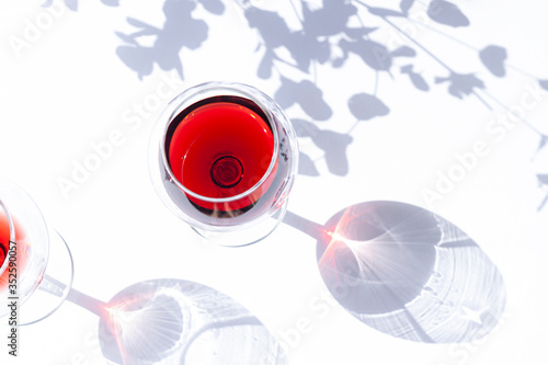 Фотография A glass of red wine on the white table with leaves shadows modern composition