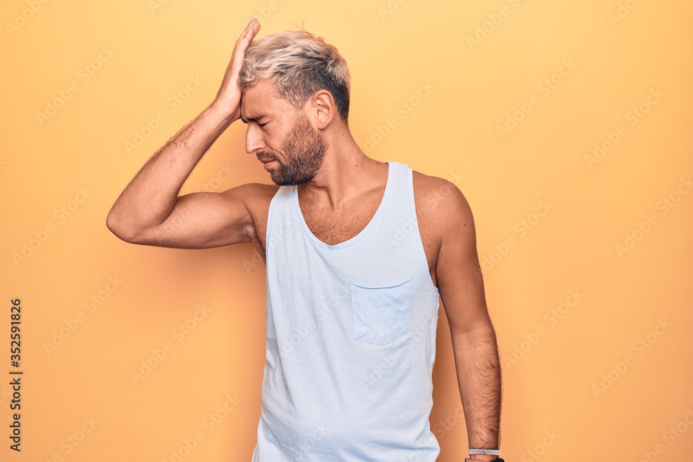 Young handsome blond man wearing casual sleeveless t-shirt over isolated yellow background surprised with hand on head for mistake, remember error. Forgot, bad memory concept. Young handsome blond man wearing casual sleeveless t-shirt over isolated yellow background surprised with hand on head for mistake, remember error. Forgot, bad memory concept.