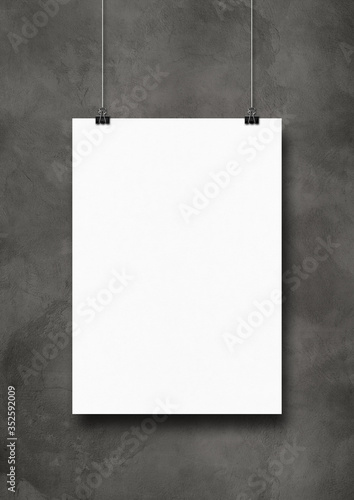 White poster hanging on a dark concrete wall with clips