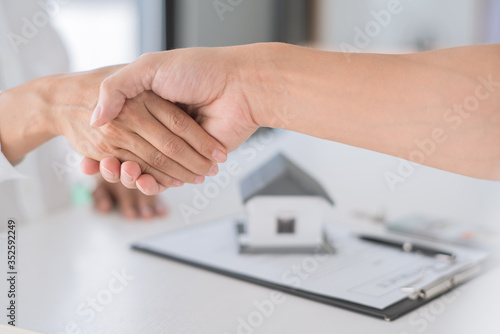 Estate agent in suit sitting in an office desk shaking hands with customer after contract signature accept agreement finish buying or rental real estate for transfer right of property.