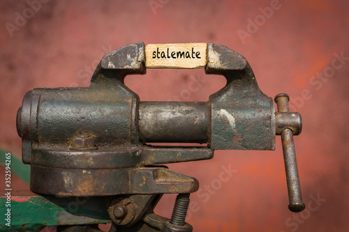 Vice grip tool squeezing a plank with the word stalemate