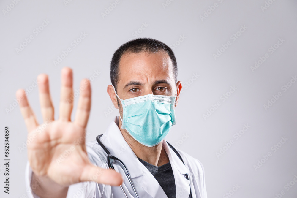 medico con camice bianco e mascherina chirurgica fa il segno di stop con la mano aperta, isolato su sfondo bianco