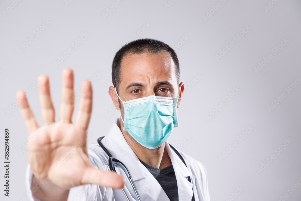 medico con camice bianco e mascherina chirurgica fa il segno di stop con la mano aperta, isolato su sfondo bianco medico con camice bianco e mascherina chirurgica fa il segno di stop con la mano aperta, isolato su sfondo bianco