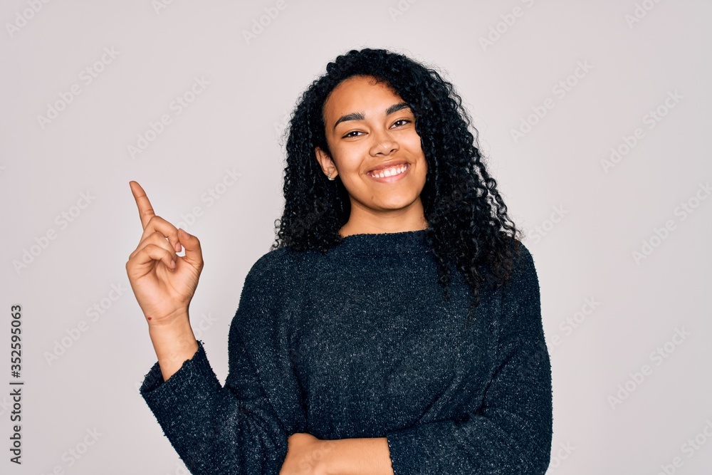 Young african american curly woman wearing casual sweater standing over white background with a big smile on face, pointing with hand and finger to the side looking at the camera. Young african american curly woman wearing casual sweater standing over white background with a big smile on face, pointing with hand and finger to the side looking at the camera.