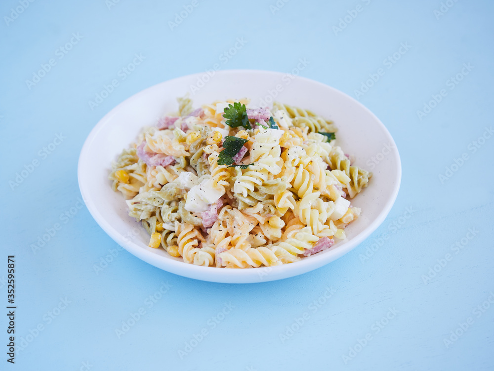 pasta salad plate with corn, cheese and jam, parsley on top, horizontal view on a blue surface with copy space pasta salad plate with corn, cheese and jam, parsley on top, horizontal view on a blue surface with copy space
