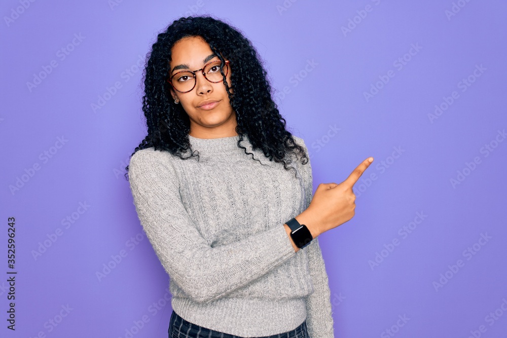 Young african american woman wearing casual sweater and glasses over purple background Pointing with hand finger to the side showing advertisement, serious and calm face