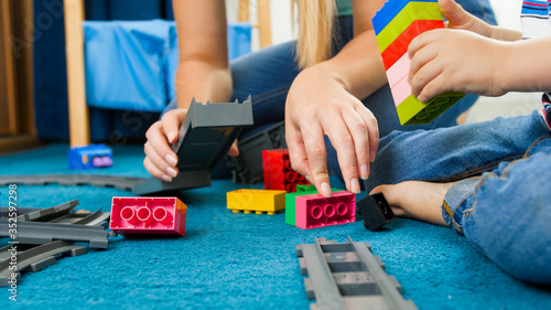 Closeup image of young caring mother helping her son building toy railroad