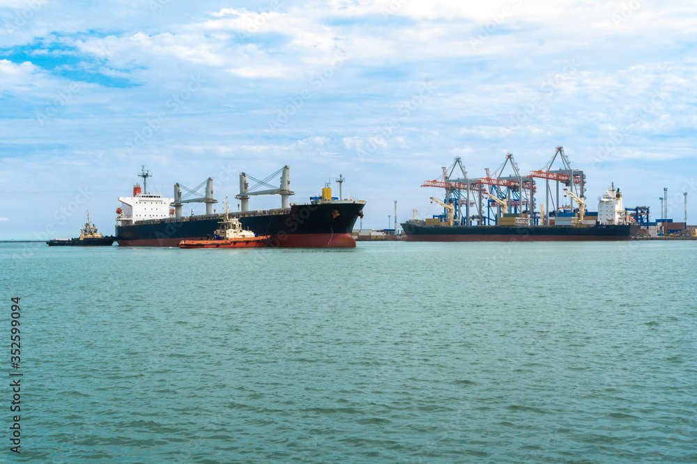 Two tugs moor the bulk carrier at the seaport. Black cargo ship mooring at the port. Cargo transportation by water. Marine business. Two tugs moor the bulk carrier at the seaport. Black cargo ship mooring at the port. Cargo transportation by water. Marine business.