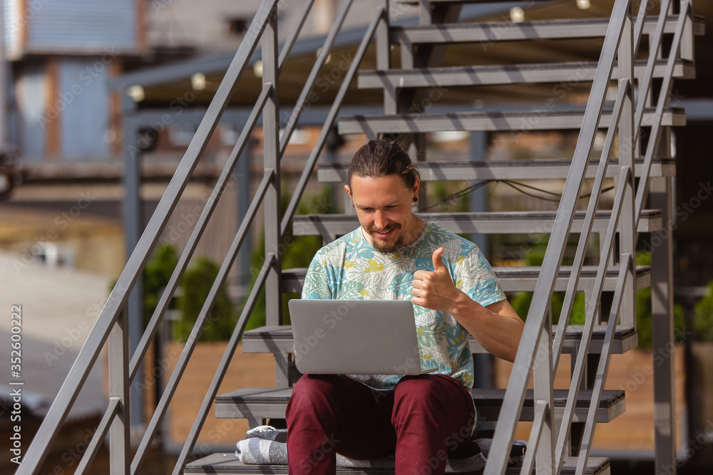 Obraz premium Thumb up. Young man, businessman working outdoors concentrated, looking on laptop screen, monitor. Copyspace for your ad. Finance, business, work, gadgets and tech concept. Freelance, remote worker.