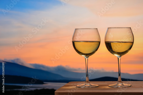 Romantic glass of wine sitting on the beach at colorful sunset. Glasses of white wine against sunset, white wine on the sky background with clouds