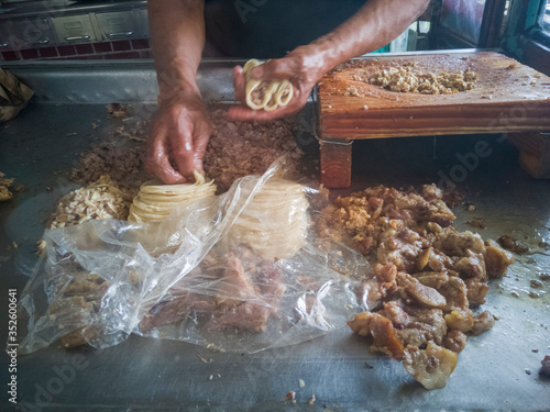 Elaboración de tacos tradicionales de diversos tipos de carnita, como barbacoa, oreja, sesos entre otros, se alcanza a ver las carnitas, la tabla de cortar carne y las manos de el taquero o cocinero. photo