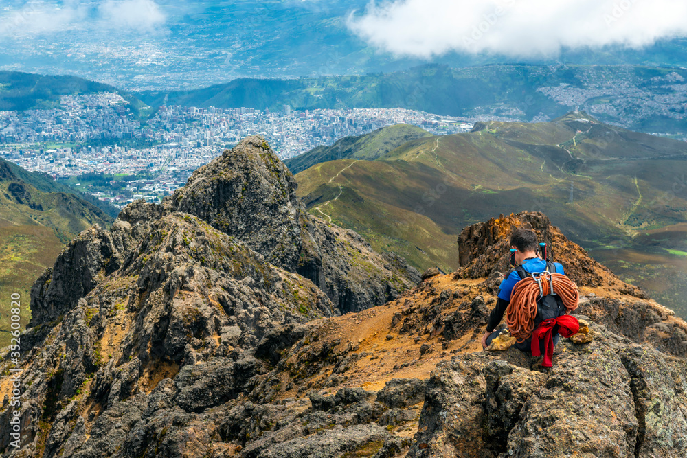 A mountain climber with ropes and walking sticks enjoying the view and making a phone call after reaching the Rucu Pichincha Volcano Peak, Quito, Ecuador.