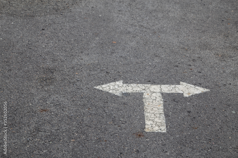 White arrow on cracked asphalt surface. Concept traffic,