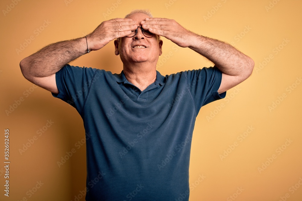Middle age handsome hoary man wearing casual polo and glasses over yellow background covering eyes with hands smiling cheerful and funny. Blind concept. Middle age handsome hoary man wearing casual polo and glasses over yellow background covering eyes with hands smiling cheerful and funny. Blind concept.