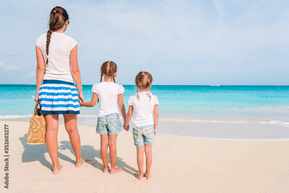 Adorable little girls and young mother on tropical white beach