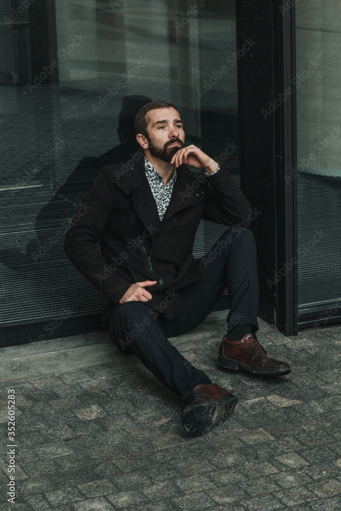 Business professional took a break from work and sit on the ground by his office building thinking. He wears brown coat, white shirt, dark trousers and brown leather boots. Business professional took a break from work and sit on the ground by his office building thinking. He wears brown coat, white shirt, dark trousers and brown leather boots.