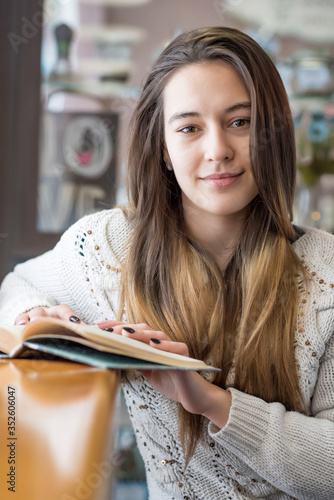 A girl with long hair is reading a book in a cafe.