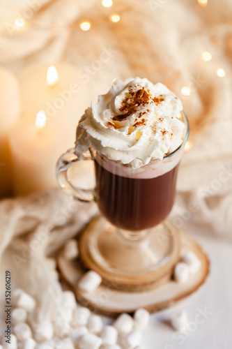 Winter hot drink: hot chocolate with marshmallow and whipped cream. Delicious sweet beverage. Christmas lights on background. Cozy home atmosphere, holiday festive mood. Close up, macro