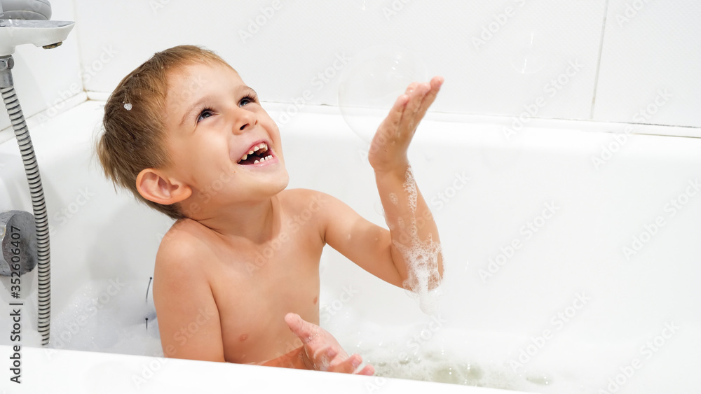 Happy smiling boy playing with soap bubbles and foam in bath Happy smiling boy playing with soap bubbles and foam in bath