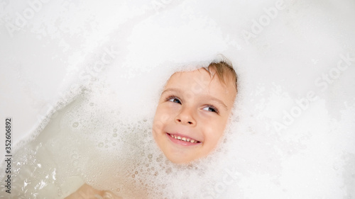 Portrait of cute smiling little boy lying in bath covered with soap foam