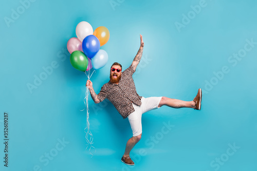 Full size photo of crazy luxury person guy hold many colorful air balloons festive event party raise hand leg wear leopard shirt sun specs shoes shorts isolated blue background photo