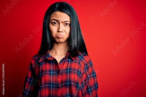 Young beautiful chinese woman wearing casual shirt over isolated red background depressed and worry for distress, crying angry and afraid. Sad expression. © Krakenimages.com