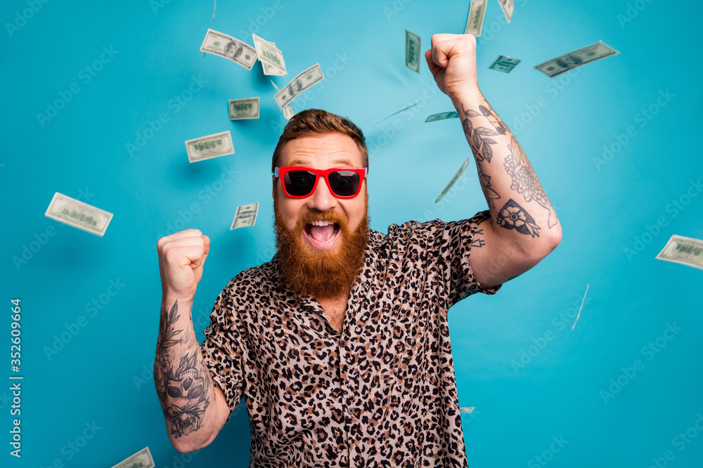 Photo of crazy handsome guy luxury rich person dollars fall from sky lottery cashback open mouth win big money raise fists wear leopard shirt sun specs isolated blue background - obrazy, fototapety, plakaty 