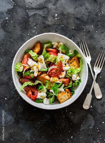 Simple rustic italian salad with fresh tomatoes, ciabatta bread, mozzarella cheese, green salad with olive oil on a dark background, top view