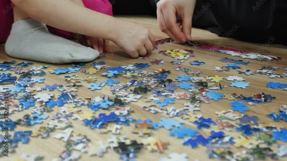 Family makes a puzzle at home on the floor. Top view, slow motion Family makes a puzzle at home on the floor. Top view, slow motion