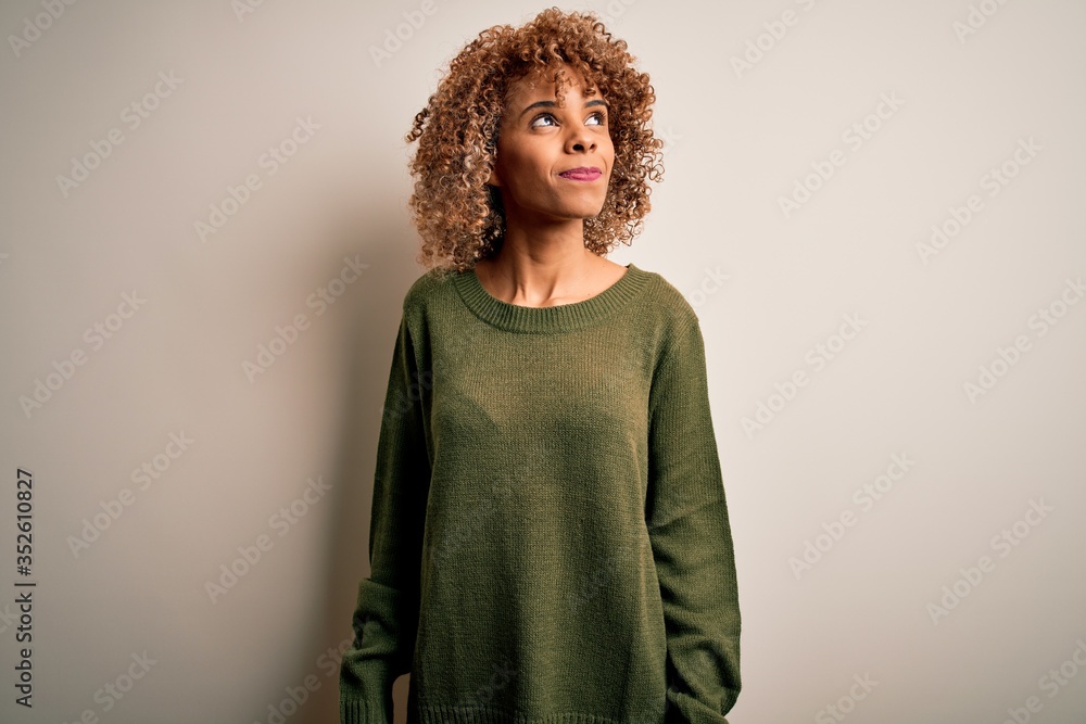 Beautiful african american woman with curly hair wearing casual sweater over white background smiling looking to the side and staring away thinking. Beautiful african american woman with curly hair wearing casual sweater over white background smiling looking to the side and staring away thinking.