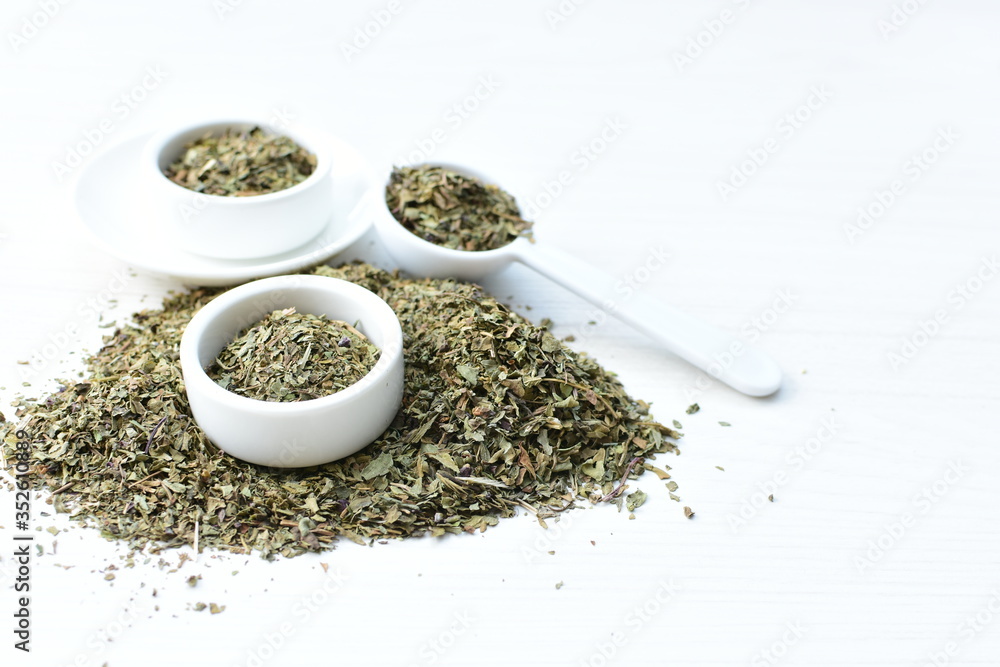 Chopped dried leaves of basil leaves on white wooden background Chopped dried leaves of basil leaves on white wooden background