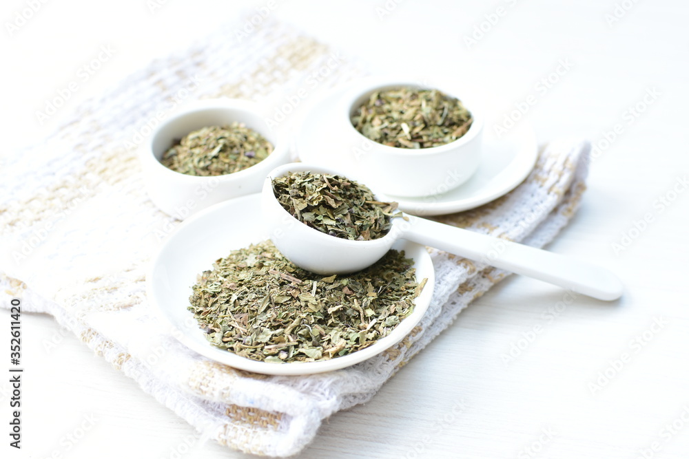 Chopped dried leaves of basil leaves on white wooden background Chopped dried leaves of basil leaves on white wooden background