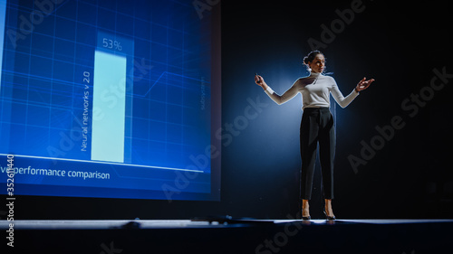 On-Stage Successful Female Speaker Presents Technological Product, Uses Remote Control for Presentation, Showing Infographics, Statistics Animation on Screen. Live Event / Device Release.