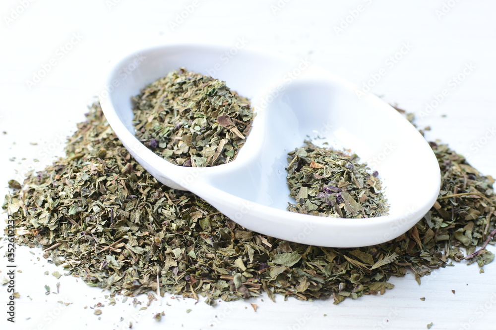Chopped dried leaves of basil leaves on white wooden background Chopped dried leaves of basil leaves on white wooden background