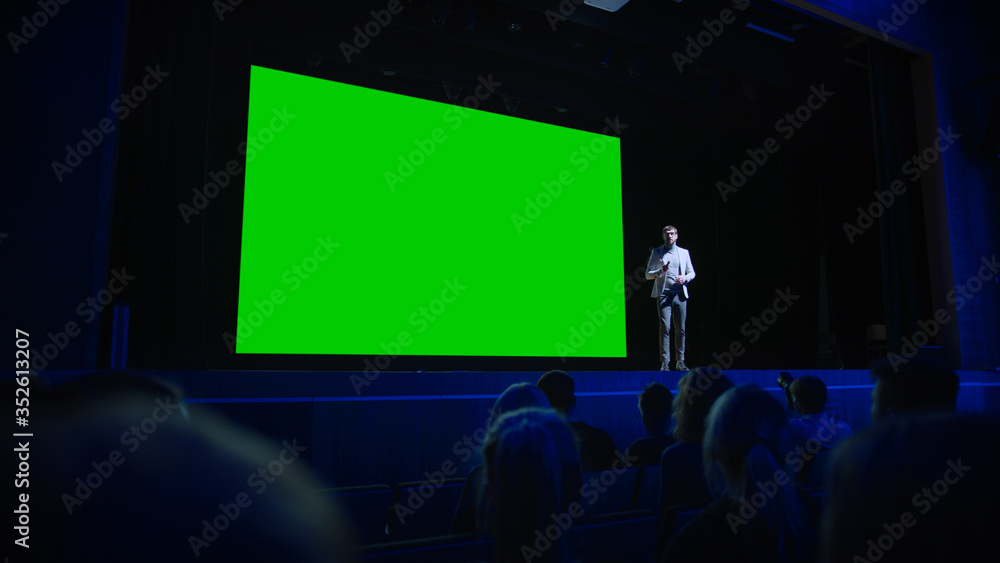 Keynote Speaker Announces New Product to the Audience, Behind Him Movie